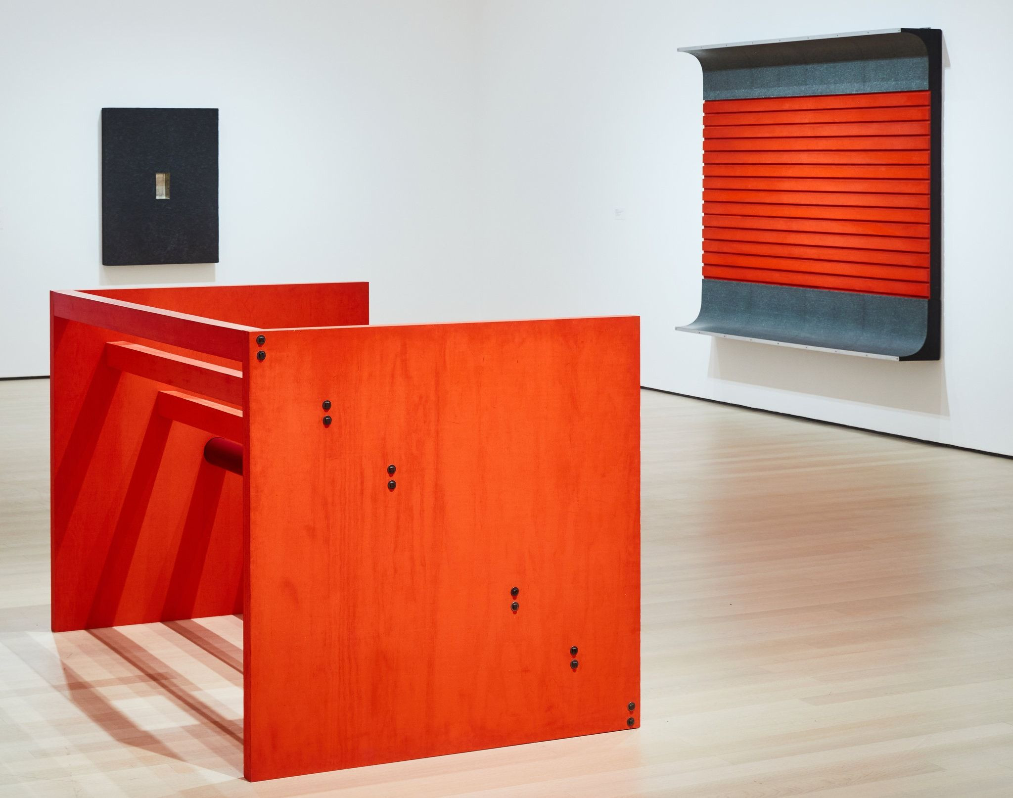An installation view showing, in the foreground, “Untitled” (1963/1975); one of Judd’s earliest experimental objects (from 1961), left, with a baking pan sunk in its surface; and, right, a 1963 piece that shows him playing with space. Donald Judd Art; Judd Foundation/Artists Rights Society (ARS), New York; Zack DeZon for The New York Times